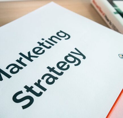 Marketing strategy document booklet with orange binding on a wooden desk beside a book